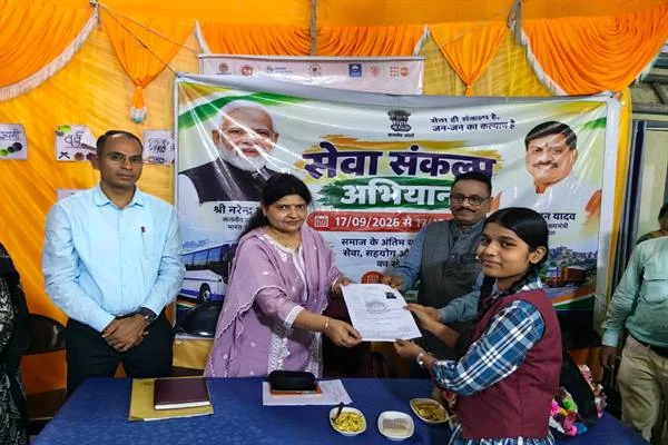 स्कूल परिसर में एक छात्रा को दस्तावेज सौंपते अधिकारी और शिक्षिका, पीछे सेवा संकल्प अभियान का बैनर लगा है